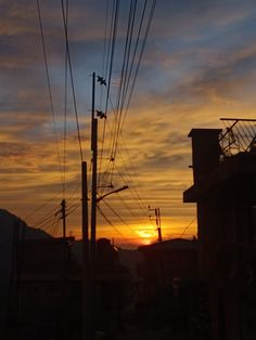 the sun is setting behind power lines and telephone poles in an urban area with buildings