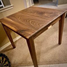 a wooden table sitting on top of a carpeted floor next to a dart board