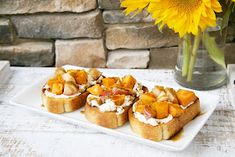 small appetizers are arranged on a plate next to a vase with sunflowers