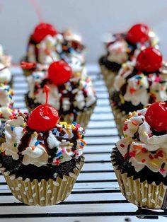 several cupcakes with cherries and sprinkles on a cooling rack