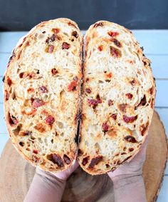 a person holding up a piece of bread on top of a wooden slice board with cheese and bacon toppings