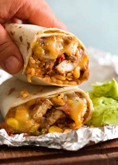 a hand is holding a burrito with meat, cheese and guacamole