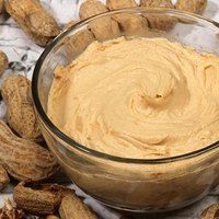 peanut butter in a glass bowl surrounded by peanuts