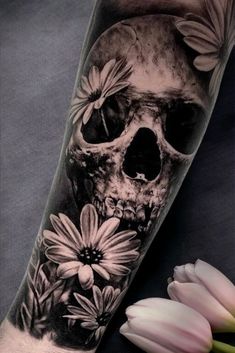 a black and white photo of a skull with flowers on it's arm, next to a tulip