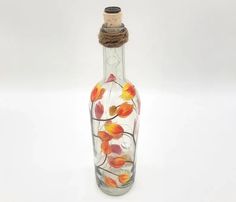 a glass bottle with flowers painted on the side and rope wrapped around the top, sitting on a white surface