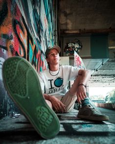 a man sitting on the ground next to a wall covered in graffiti