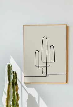 a plant sitting next to a white wall with a black line drawing on the wall