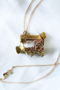 an old sewing machine necklace on a white sheet with a gold plated chain hanging from it