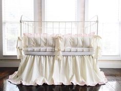 a white crib with pink ruffles and pillows