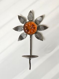 a metal clock with an orange flower and leaves on it's face, hanging from a wall