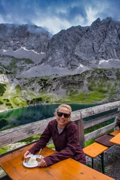 a woman sitting at a picnic table in front of mountains