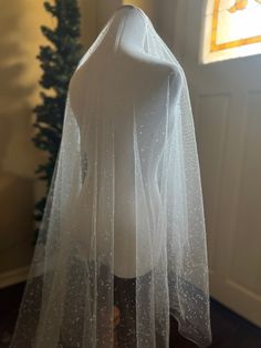 a white wedding veil on display in front of a window with a christmas tree behind it