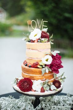 a multi layer cake with flowers and berries on top is sitting on a black table