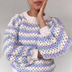 a woman wearing a crocheted sweater and holding her hand to her face