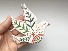 a hand holding a white bird ornament with green and red designs on it