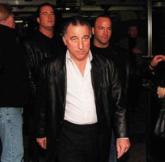 a group of men standing around each other in front of a man wearing a black leather jacket