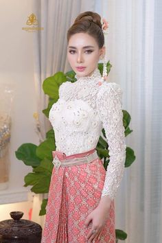 a woman in a white top and pink skirt standing next to a cake on a table