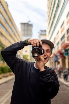 a man holding a camera up to his face while standing on the side of a road