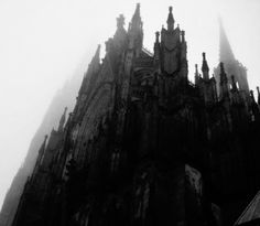 the top of a tall building with spires on it's sides and fog in the air