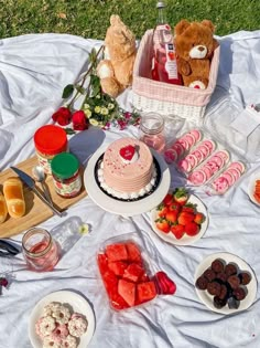 a picnic table with cake, fruit and other food items on the blanket outside in the grass