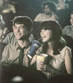 a man and woman sitting next to each other in front of a movie screen holding drinks