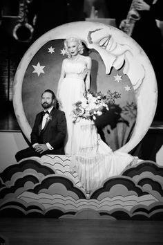 a man and woman standing next to each other in front of a large moon sculpture