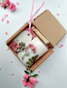 two white candles in a box with pink flowers