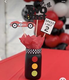 a red table topped with a black vase filled with cake toppers and paper cars