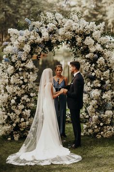 a bride and groom standing in front of a floral arch