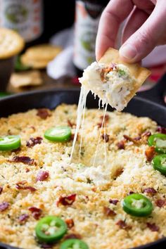 a person is dipping cheese into a skillet filled with green peppers and cheesy bread