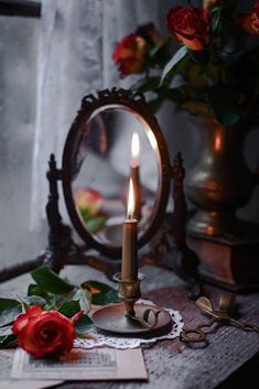 a candle on a table with roses and an old mirror in the backround