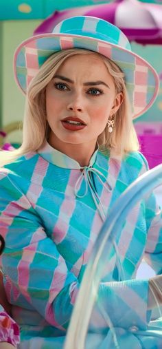 a woman with blonde hair wearing a blue and pink checkered shirt, hat and hoop earrings