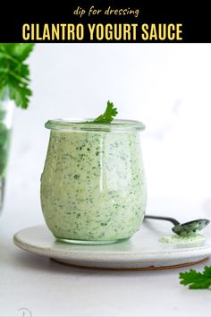 a small glass jar filled with cilantro yogurt sauce on top of a white plate