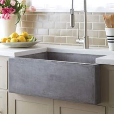 a kitchen sink sitting under a window next to a bowl of fruit and utensils