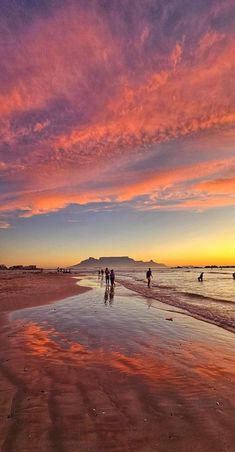 people walking on the beach at sunset with pink clouds in the sky and blue water