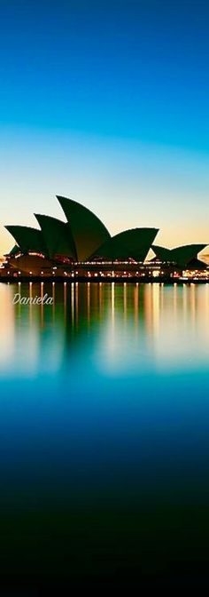 the sydney opera house is lit up at night with lights reflecting in the water below