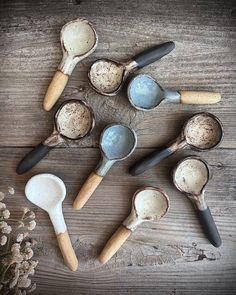 six spoons are lined up next to each other on a wooden surface with flowers in the background