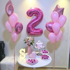 a table topped with pink balloons and cupcakes next to a number two sign