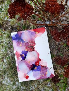 a piece of paper with flowers painted on it sitting in the grass next to snow