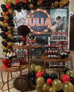 a table topped with lots of desserts under a balloon filled arch in front of a movie poster