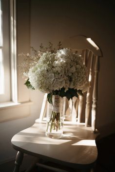 a bouquet of white flowers sitting on top of a wooden chair next to a window