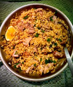 a pan filled with rice and meat on top of a green table cloth next to a spoon