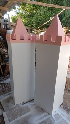 two tall white towers with pink tops sitting on top of a cement slab in front of a tree