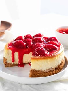 a cheesecake with strawberries on top is sitting on a plate next to another dessert