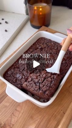 a brownie baked in a white dish with a wooden spatula