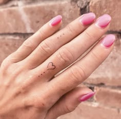 a woman's hand with a small heart tattoo on her left index finger and pink nail polish