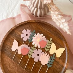 some paper flowers and butterflies on a wooden plate