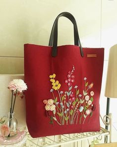 a red handbag with flowers on it sitting on a shelf next to a lamp