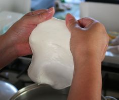 two hands are holding a large ball of white dough over a stove top burner