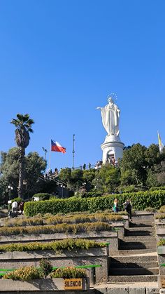 there are many steps that lead up to the statue on top of a hill in front of some trees